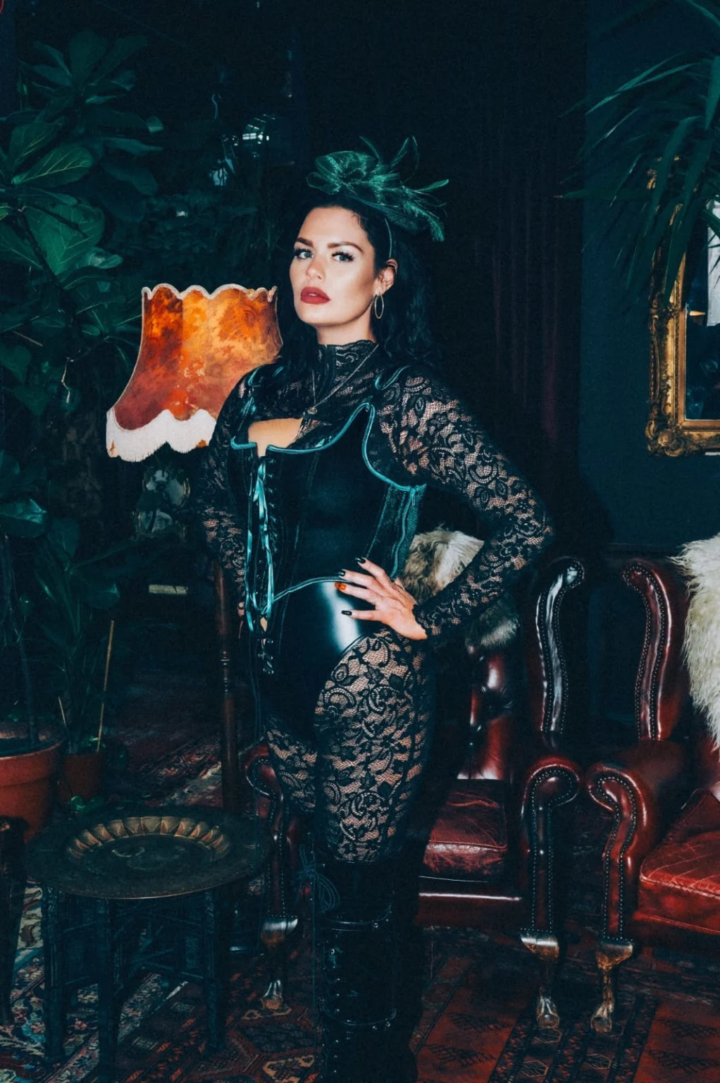 Mistress Charlotte O’Winter standing beside an amber lamp in a leather corset and black lace