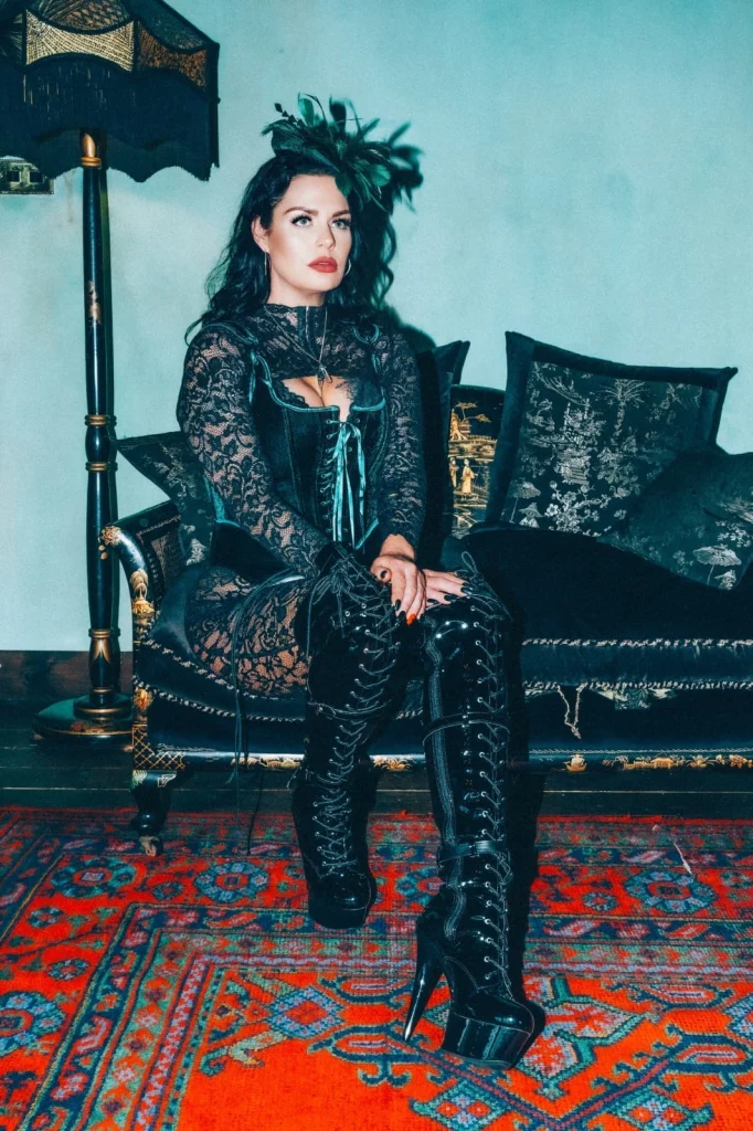 Mistress Charlotte, professional dominatrix, seated on a sofa in lace and leather boots