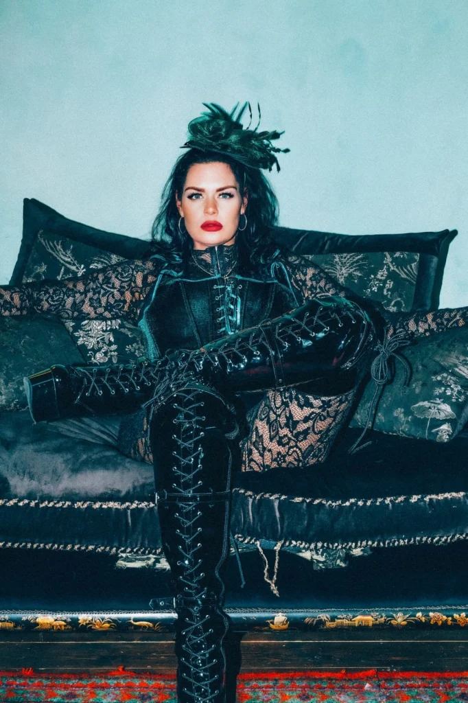 London dominatrix Mistress Charlotte seated on a black velvet sofa in lace and lace-up boots