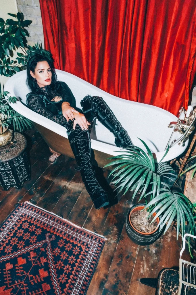 Mistress Charlotte O’Winter reclining in a clawfoot bath in black lace and thigh-high boots