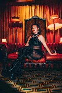 Mistress Charlotte, London dominatrix, seated on a red leather throne in latex boots