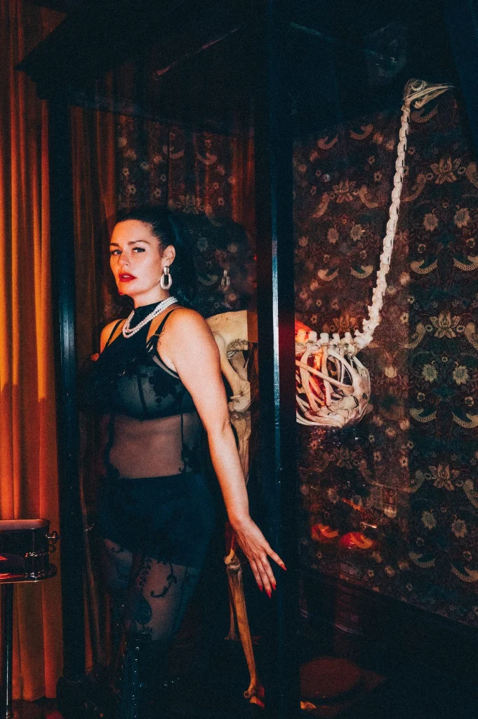 Mistress Charlotte O’Winter beside coiled bondage rope in a candlelit dungeon