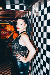 Mistress Charlotte O’Winter in lace and latex against a chequered wall, chastity mistress in London