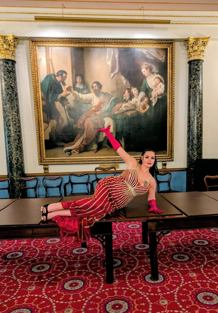 Mistress Charlotte O’Winter reclining in a red gown in a grand salon