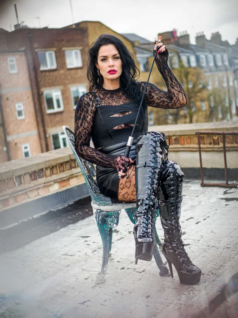 Mistress Charlotte O’Winter seated with a riding crop on a London rooftop, caning mistress